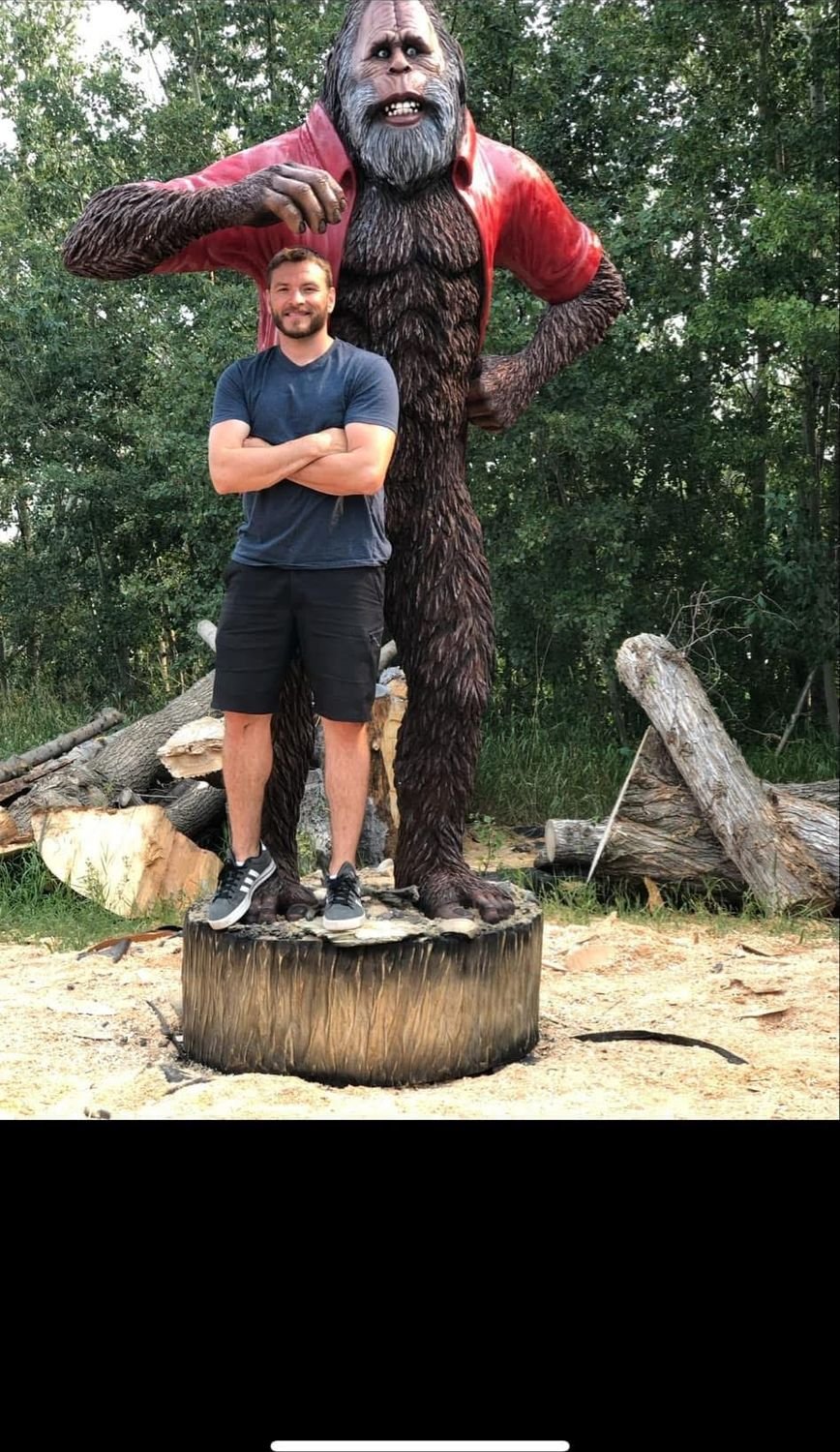 A tall carved figure of a bearded man with a person standing in front of it.