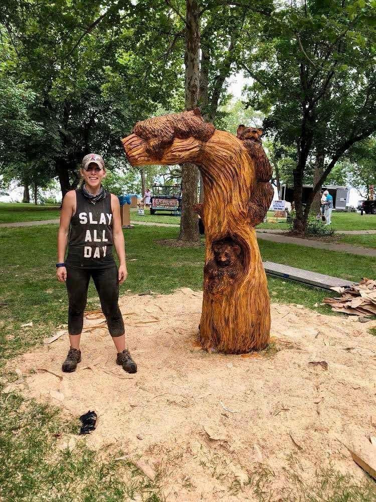 A carved bear sculpture in a tree trunk with the artist standing beside it.